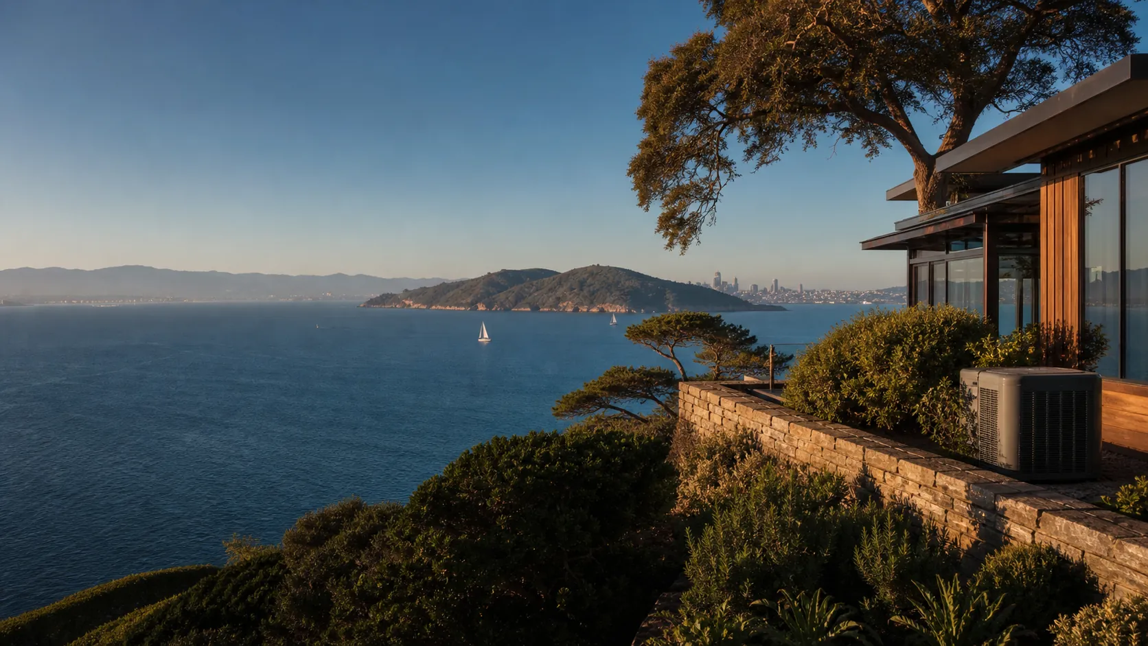 Luxury hillside home overlooking San Francisco Bay in Tiburon with a discreet modern air-conditioning condenser beside a landscaped terrace at golden hour.